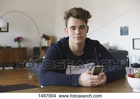 Picture - Portrait of teenage boy sitting at table with smart phone. Fotosearch
