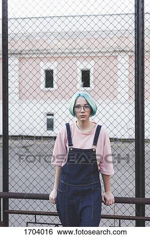 Stock Photograph - Portrait of teenage girl standing by fence in city. Fotosearch