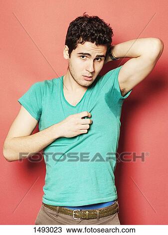 Stock Image - Portrait of tired man showing sweaty t-shirt against red background. Fotosearch