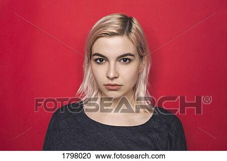 Stock Image - Portrait of woman with bleached hair and serious expression against red background. Fotosearch