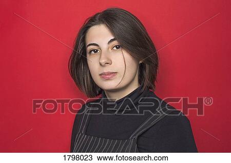 Stock Image - Portrait of woman with dark hair and serious expression against red background. Fotosearch
