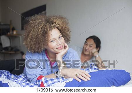 Portrait of young couple lying on bed with hands on chin against white wall at home View Large Photo Image Stock Photography - Portrait of young couple lying on bed with hands on chin against white wall at home. Fotosearch
