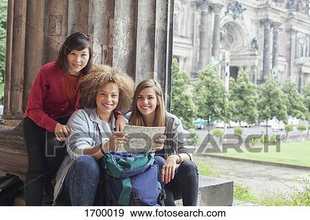 Stock Photo - Portrait of young female tourists sitting with map at Altes Museum against Berlin Cathedral, Germany. Fotosearch
