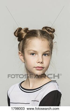 Stock Image - Portrait of young girl with double hair buns against grey background. Fotosearch