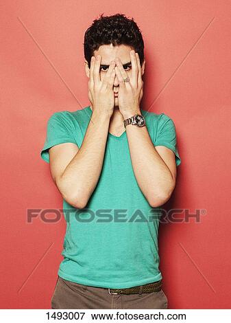 Stock Photo - Portrait of young man covering face with hands against red background. Fotosearch