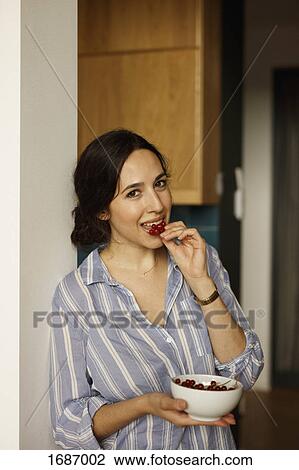 Stock Image - Portrait of young woman eating red currants at home. Fotosearch