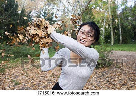 Portrait of young woman throwing dry leaves while standing at park during autumn View Large Photo Image Stock Photograph - Portrait of young woman throwing dry leaves while standing at park during autumn. Fotosearch