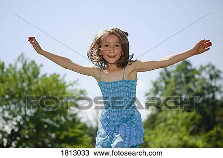 Stock Image - Portrait playful girl with arms outstretched jumping for joy in sunny yard. Fotosearch