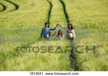 Stock Image - Portrait pregnant family in sunny, idyllic rural green field with wildflowers. Fotosearch