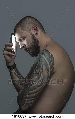 Stock Photo - Portrait serious bare chested man with tattoos holding smart phone. Fotosearch