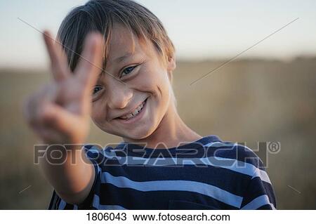 Stock Image - Portrait smiling, carefree boy gesturing peace sign. Fotosearch