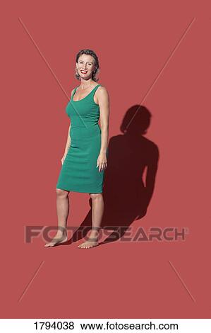 Stock Photo - Portrait smiling, confident barefoot woman in green dress against red background. Fotosearch