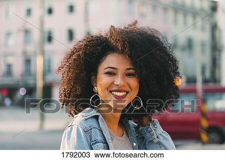 Stock Image - Portrait smiling, confident young woman on urban street. Fotosearch