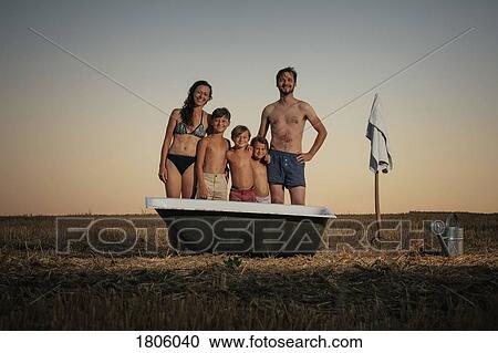 Stock Image - Portrait smiling family in bathing suits standing next to bathtub in rural field. Fotosearch