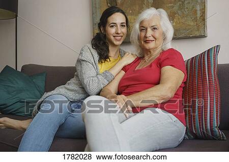 Stock Photo - Portrait smiling senior mother sitting with daughter on living room sofa. Fotosearch