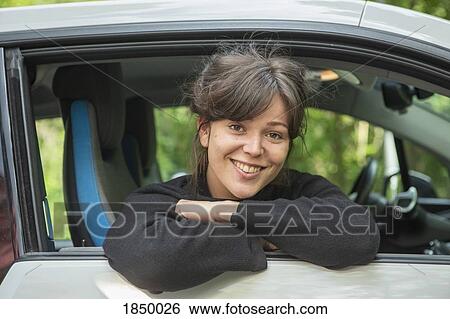 Stock Photograph - Portrait smiling young woman leaning out car window. Fotosearch