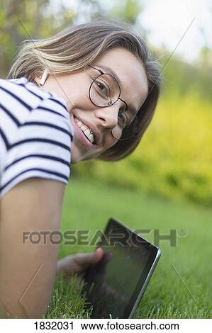 Stock Image - Portrait smiling young woman with digital tablet and headphones in grass. Fotosearch