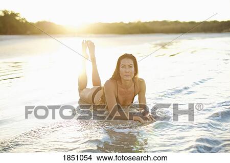 Picture - Portrait woman in bikini laying in sunny ocean surf. Fotosearch
