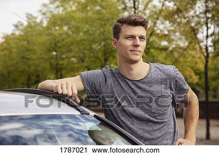 Stock Image - Portrait young man leaning on car, looking away. Fotosearch