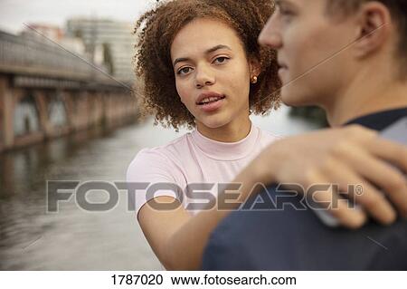 Stock Image - Portrait young woman hugging boyfriend at riverside. Fotosearch