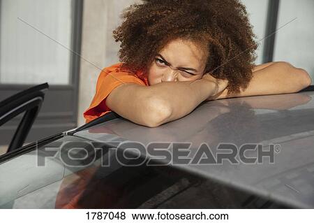 Portrait young woman squinting, leaning on car View Large Photo Image Stock Photo - Portrait young woman squinting, leaning on car. Fotosearch