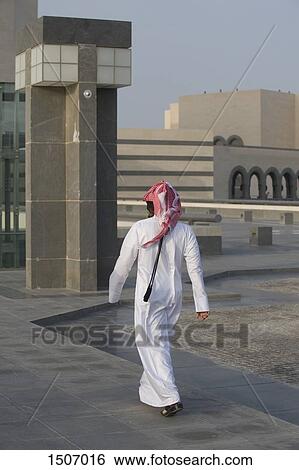 Rear view of Arab man walking on floor against buildings View Large Photo Image Stock Photograph - Rear view of Arab man walking on floor against buildings. Fotosearch