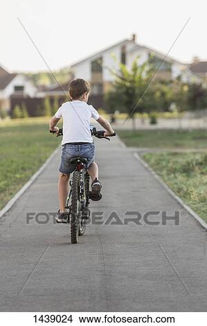 Rear view of boy cycling on footpath View Large Photo Image Picture - Rear view of boy cycling on footpath. Fotosearch