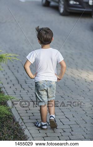 Rear view of boy with hands on hip standing on street View Large Photo Image Stock Photo - Rear view of boy with hands on hip standing on street. Fotosearch