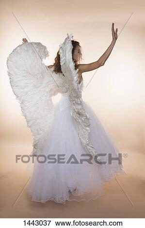 Stock Photo - Rear view of bride wearing angel wings while standing against colored background. Fotosearch