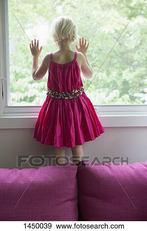 Stock Photo - Rear view of girl standing on sofa by window at home. Fotosearch