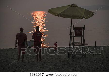 Rear view of lifeguards standing at beach during sunset View Large Photo Image Stock Photo - Rear view of lifeguards standing at beach during sunset. Fotosearch