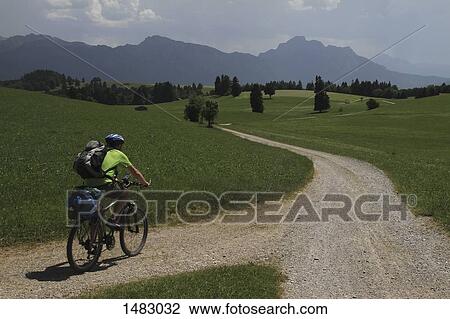 Rear view of man riding bicycle on road amidst grassy field against sky View Large Photo Image Stock Image - Rear view of man riding bicycle on road amidst grassy field against sky. Fotosearch