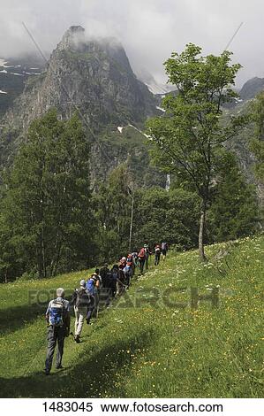 Rear view of people walking on grassy field against mountains View Large Photo Image Stock Photography - Rear view of people walking on grassy field against mountains. Fotosearch