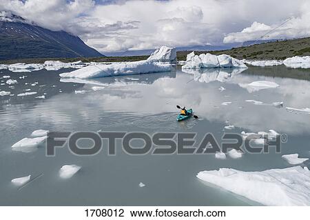 Stock Image - Rear view of person canoeing lagoon against cloudy sky, Lake George, Palmer, Alaska. Fotosearch