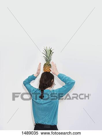 Rear view of woman balancing pineapple while standing against white background View Large Photo Image Stock Photography - Rear view of woman balancing pineapple while standing against white background. Fotosearch