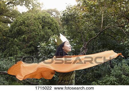 Stock Image - Rear view of woman wearing crown and orange scarf against trees at park. Fotosearch
