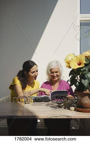 Senior mother and daughter reading magazine on sunny patio View Large Photo Image Picture - Senior mother and daughter reading magazine on sunny patio. Fotosearch