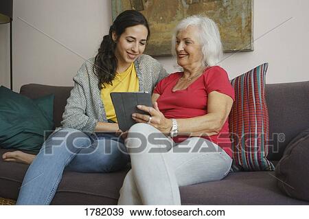 Stock Photo - Senior mother and daughter using digital tablet on living room sofa. Fotosearch