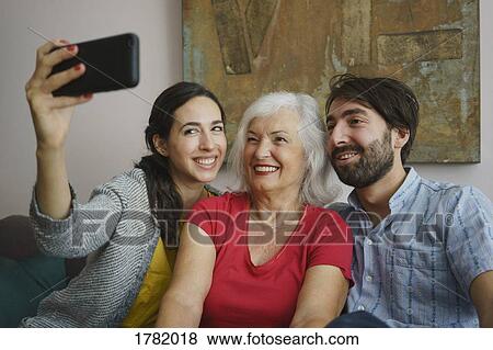 Stock Photo - Senior mother taking selfie with daughter and son. Fotosearch