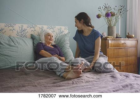 Stock Photo - Senior mother talking with daughter on bed. Fotosearch