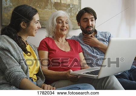 Picture - Senior mother using laptop with daughter and son on living room sofa. Fotosearch