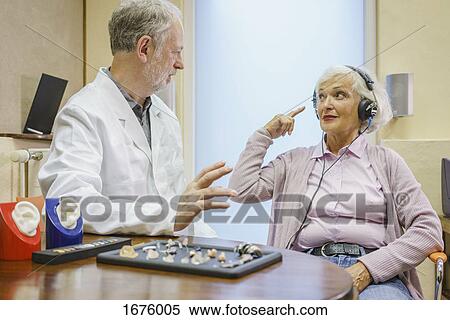Stock Photography - Senior patient wearing headphones talking to Audiologist during ear exam at doctor's office. Fotosearch