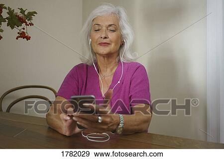 Stock Photo - Senior woman listening to music with headphones and mp3 player. Fotosearch