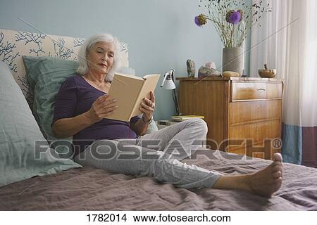 Picture - Senior woman reading book on bed. Fotosearch