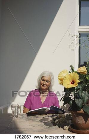 Senior woman reading magazine on sunny patio View Large Photo Image Stock Photo - Senior woman reading magazine on sunny patio. Fotosearch