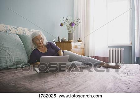 Senior woman using laptop on bed View Large Photo Image Stock Photography - Senior woman using laptop on bed. Fotosearch