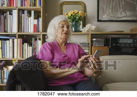 Senior woman using smart phone on living room sofa View Large Photo Image Stock Photo - Senior woman using smart phone on living room sofa. Fotosearch