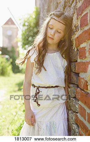 Stock Photo - Serene girl in dress leaning against brick wall. Fotosearch