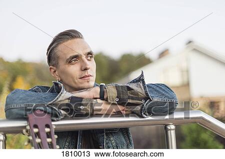 Stock Image - Serene man leaning on railing and looking away. Fotosearch