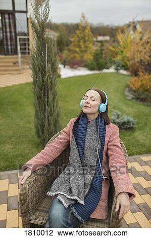 Serene woman in scarf and coat listening to music with headphones on autumn patio View Large Photo Image Stock Image - Serene woman in scarf and coat listening to music with headphones on autumn patio. Fotosearch